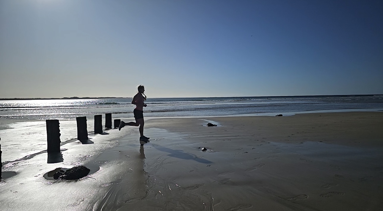 A runner moving along a wide Welsh beach
